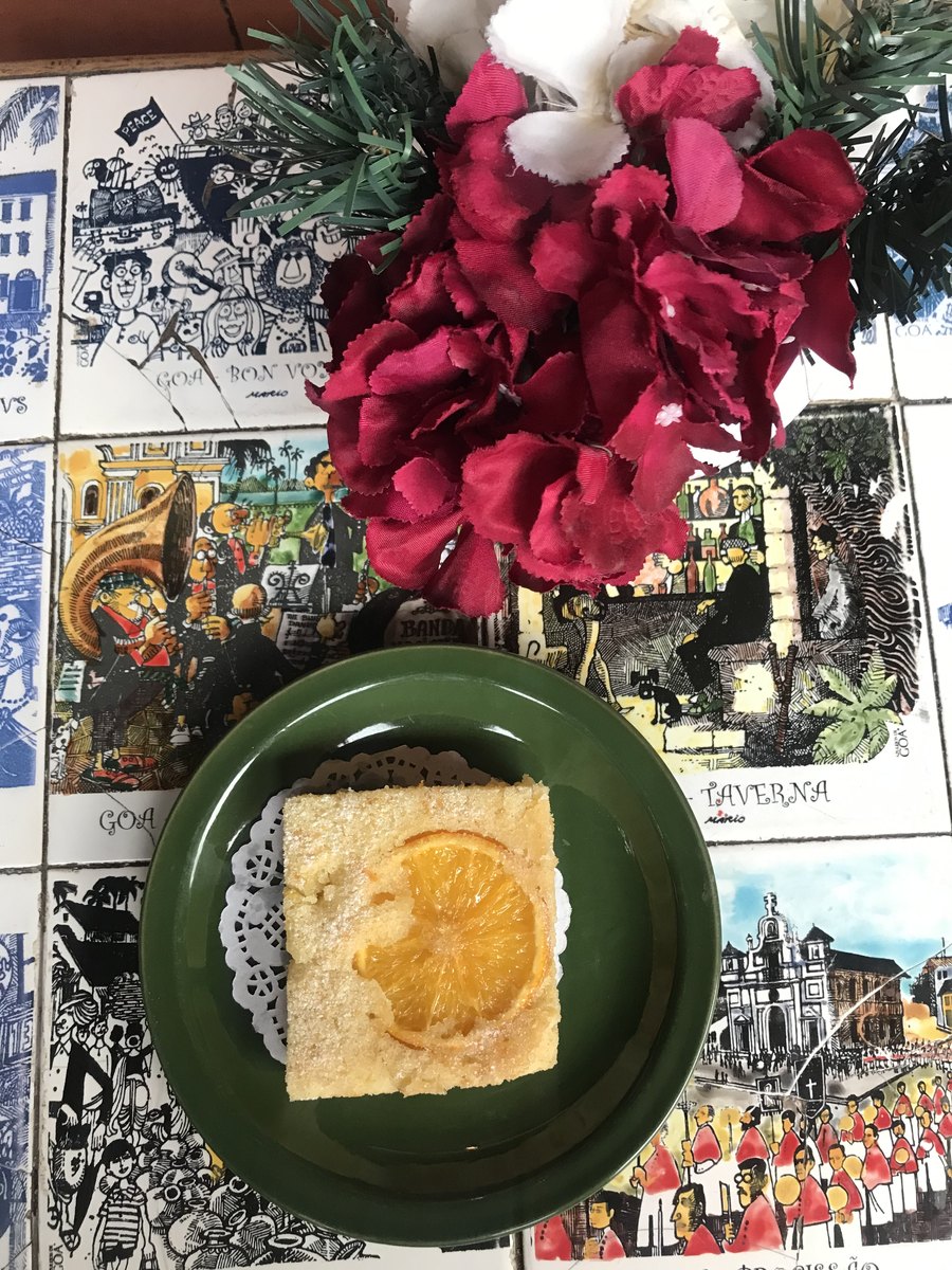 A slice of orange cake on a green plate over illustrated ceramic tiles