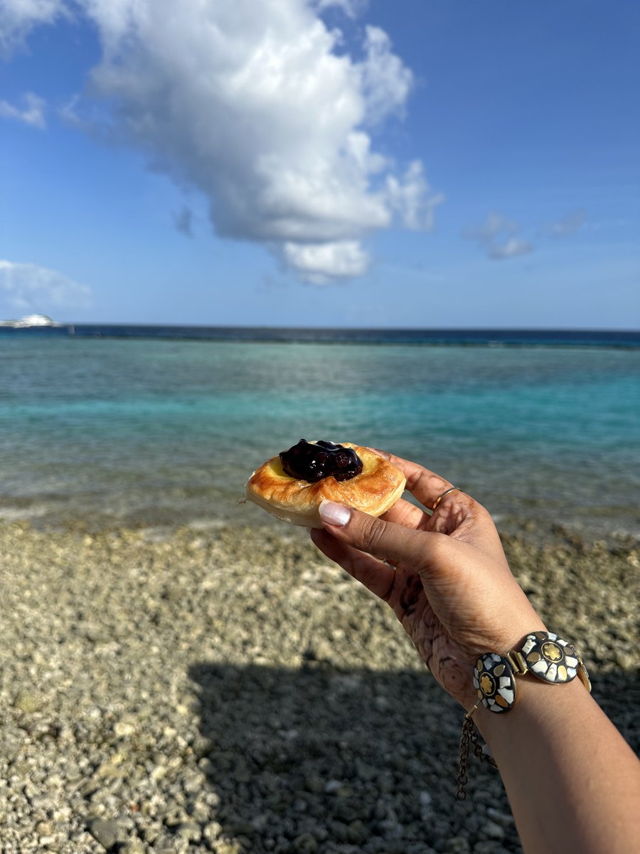 A hand holding a berry pastry up against a turquoise sea and sky