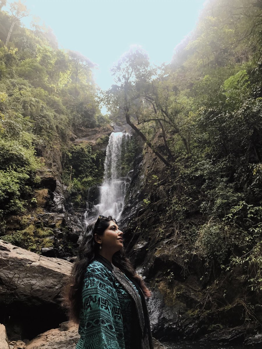 Ayesha gazing upward in front of a waterfall in a green forest